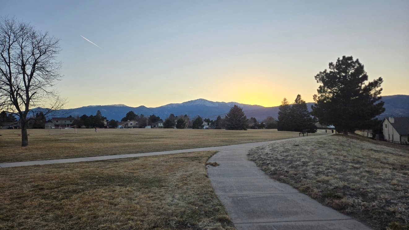 A paved walking path through open grassland toward the mountains at sunrise