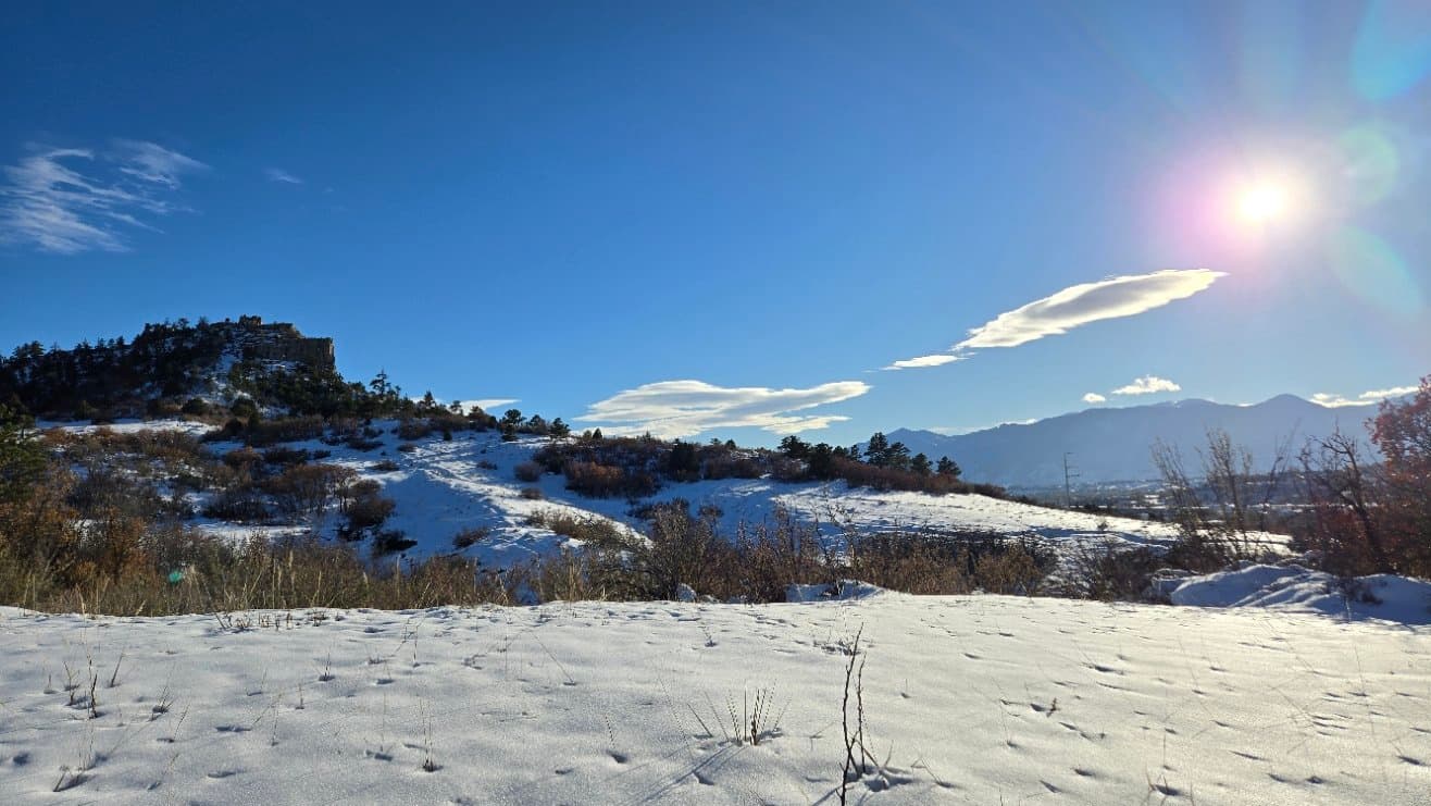 Sun shining over a snow-covered meadow with mountains in the distance