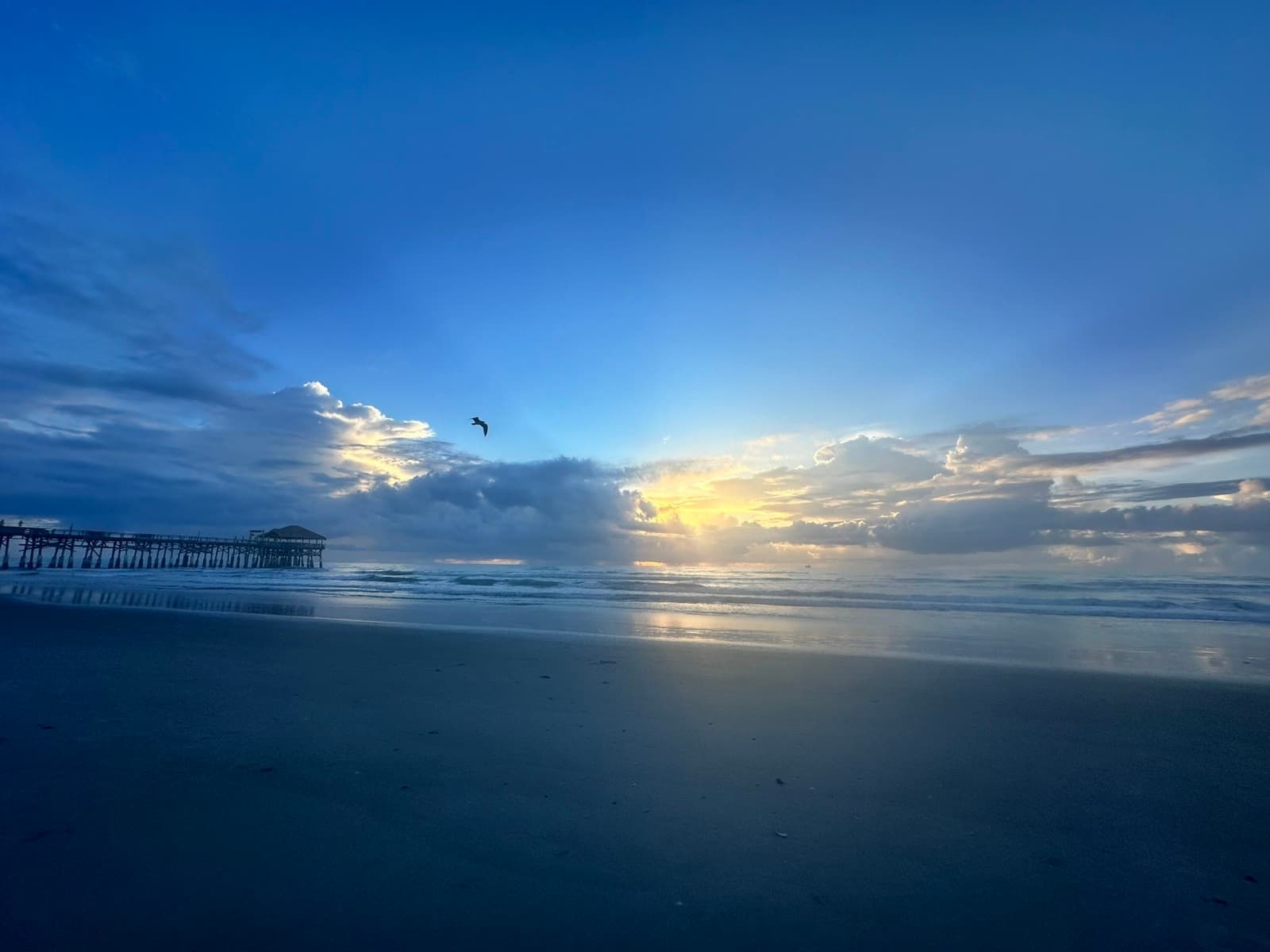 Sunlight breaking through clouds over the ocean beside a pier