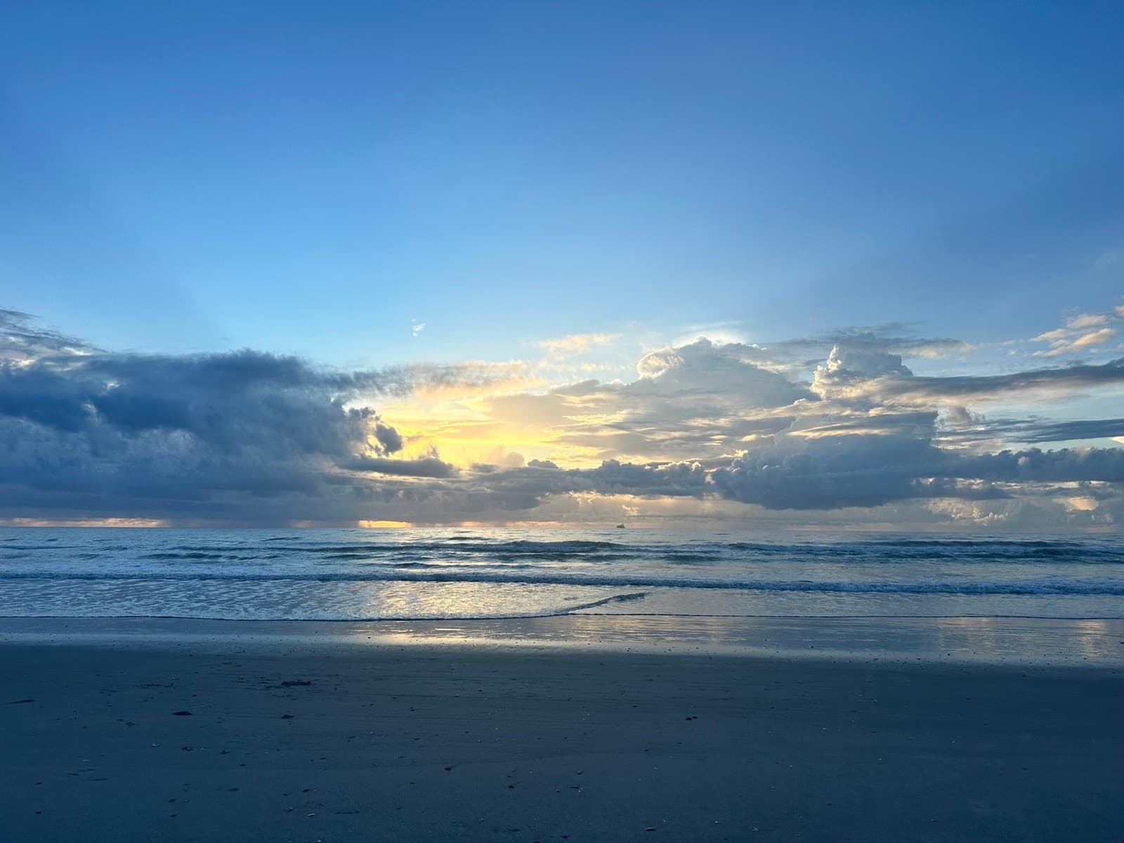 The sun rising behind clouds over a quiet beach