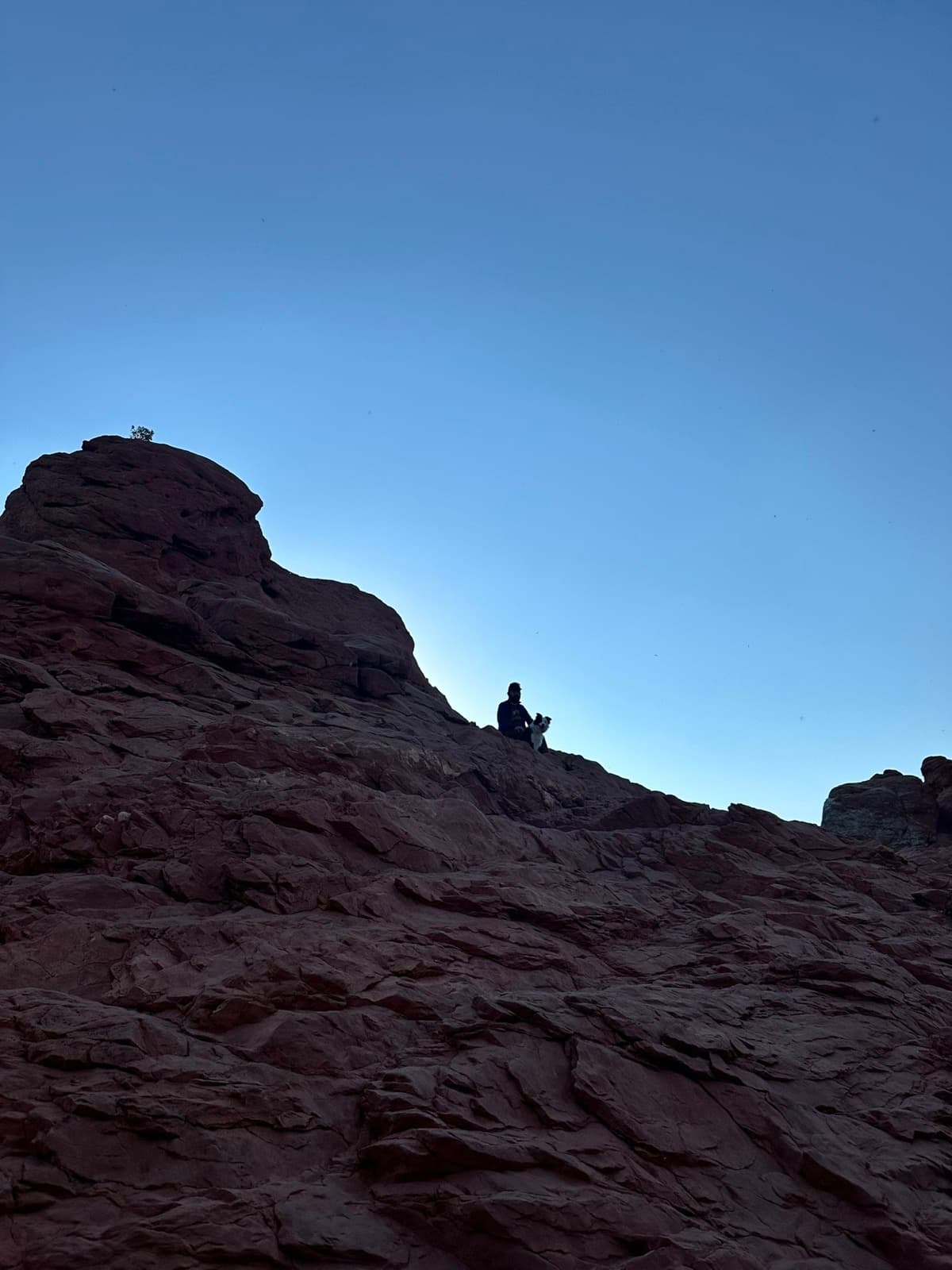 A person sitting quietly on top of a red rock formation against a blue sky
