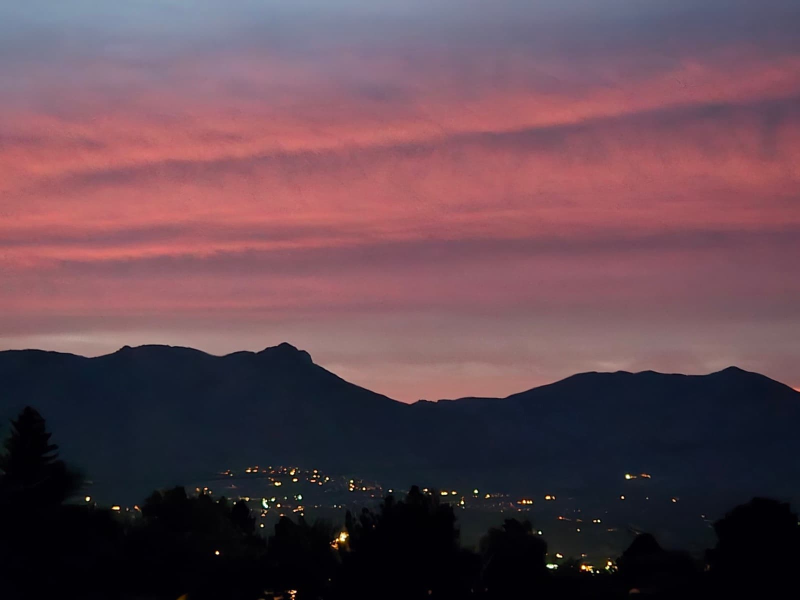 Pink clouds at dusk over dark mountains and city lights