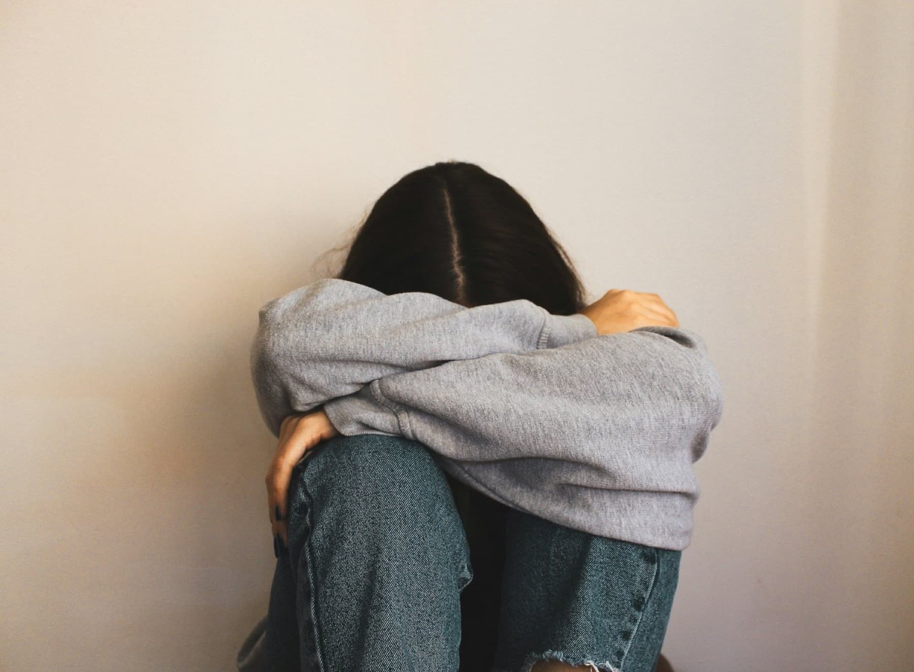 A woman sitting against a wall, holding her knees close
