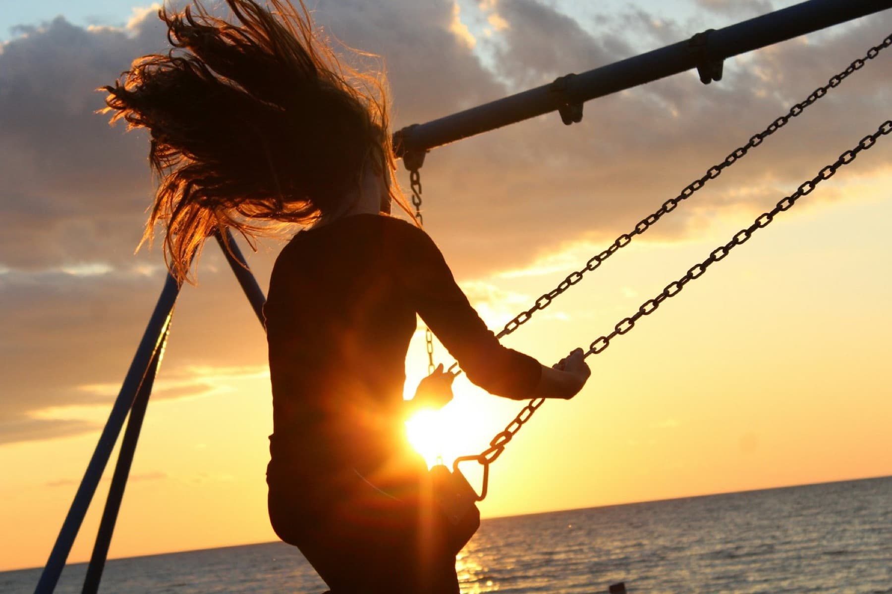 A woman swinging freely at sunset over the water