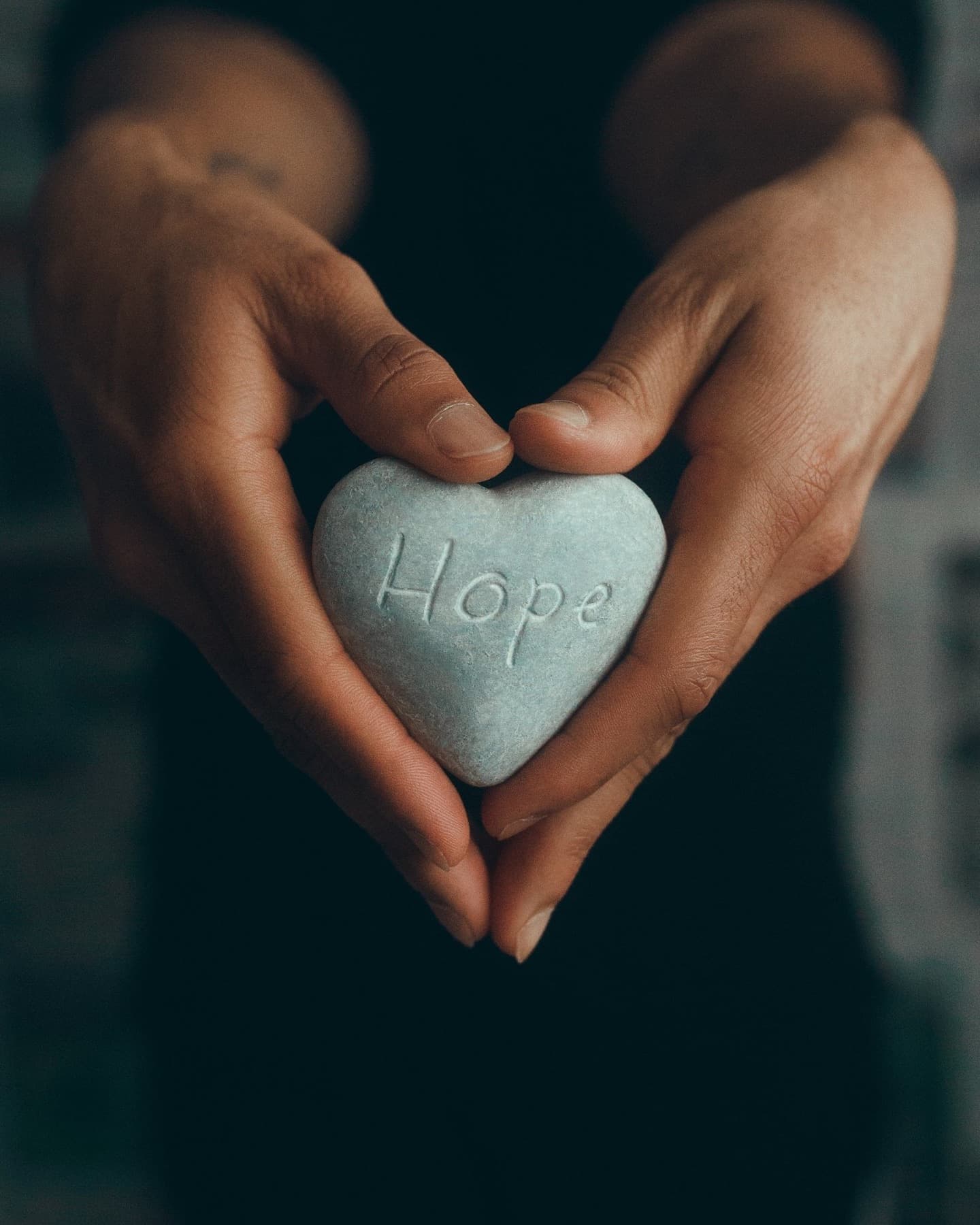 Hands holding a heart-shaped stone engraved with the word hope