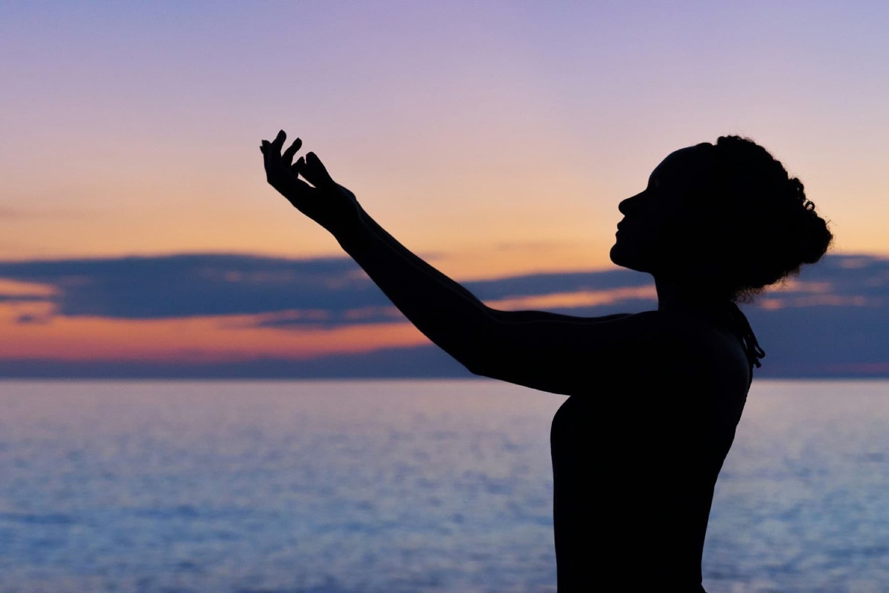 A woman reaching toward the sky at dusk by the sea