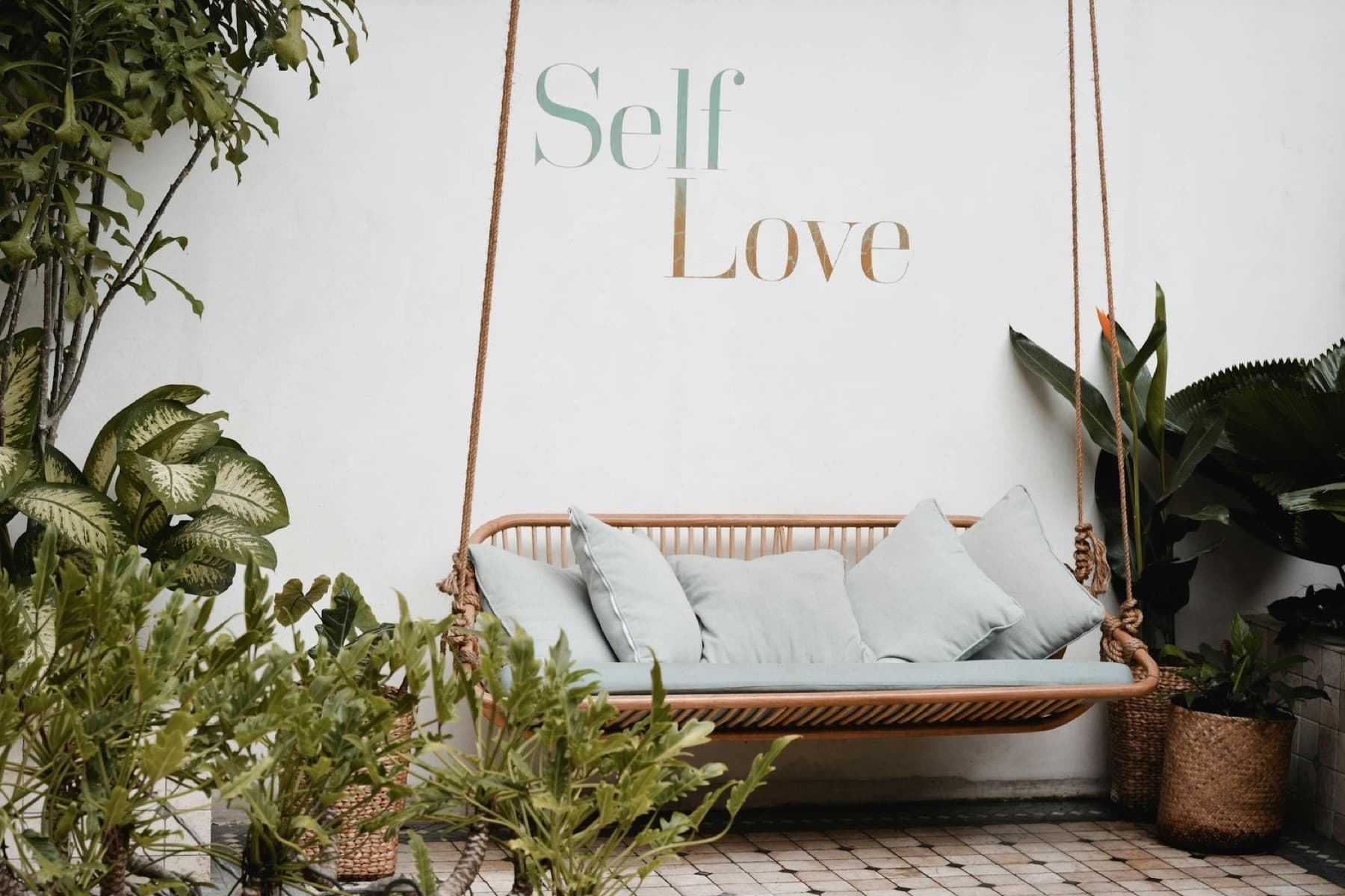 A bright room with a hanging swing and the words Self Love on the wall